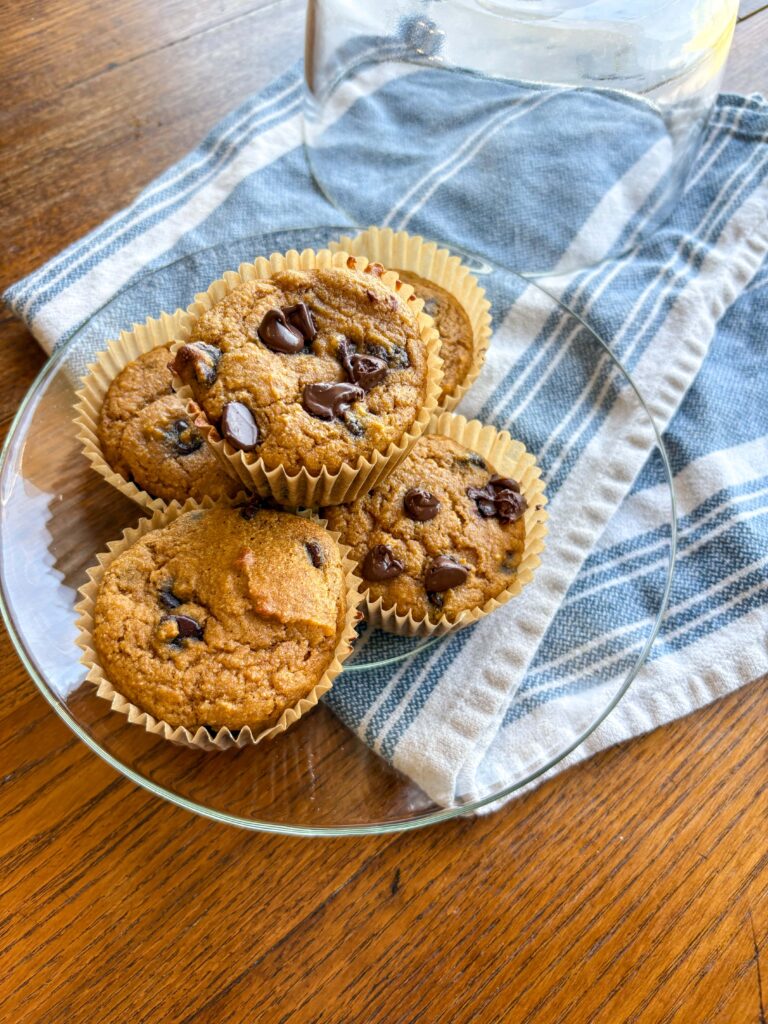 pumpkin chocolate chip muffins on a glass plate on a tea towel on a wooden table