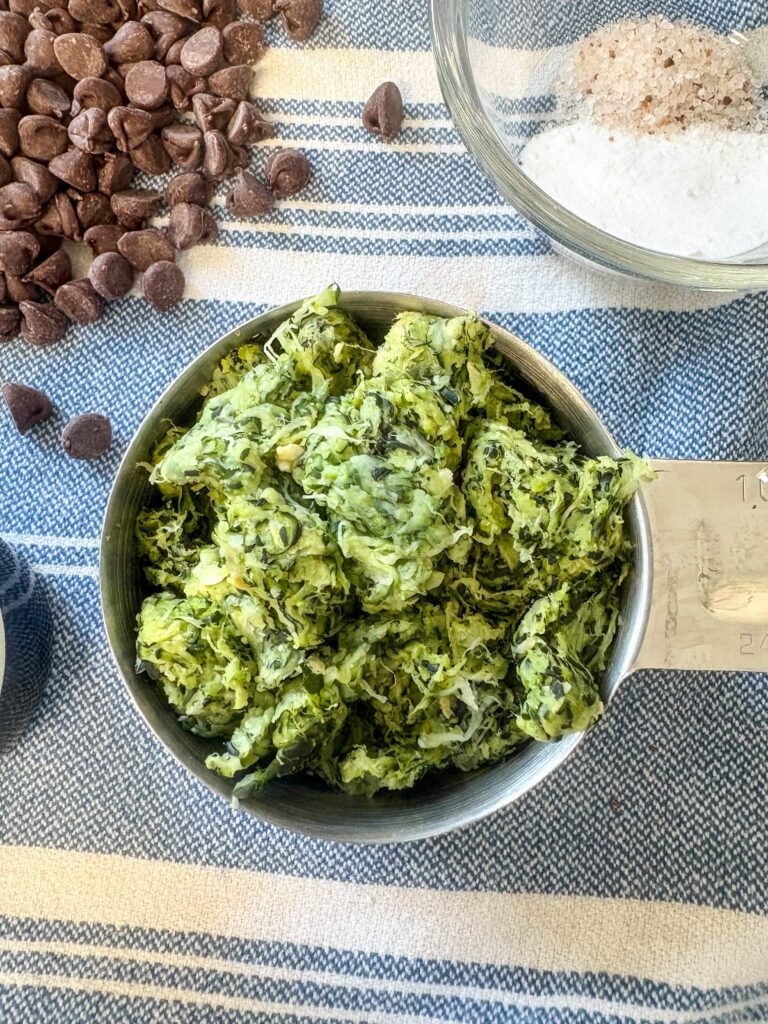 shredded zucchini on a tea towel in a stainless steel cup