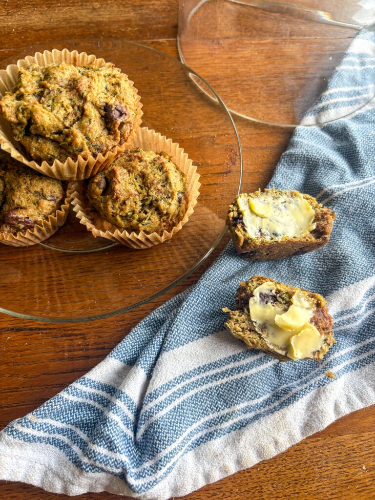zucchini muffins on a glass plate on a kitchen table with a blue and white pinstripe tea towel