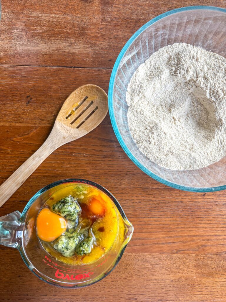 ingredients for zucchini muffin batter in a glass bowl with a wooden spoon on a kitchen table