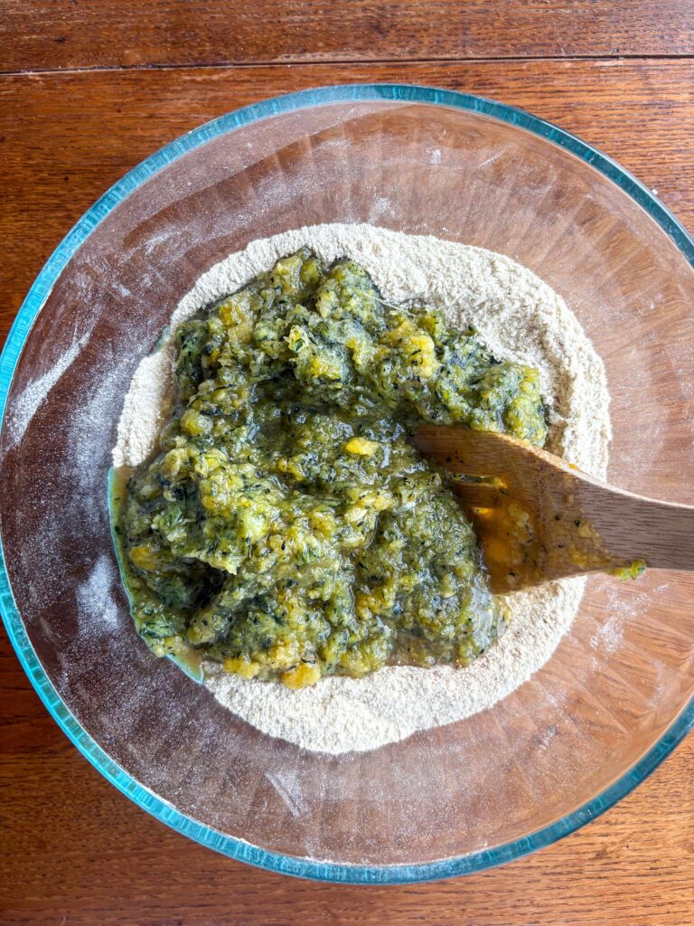 zucchini muffin batter in a glass bowl with a wooden spoon on a kitchen table