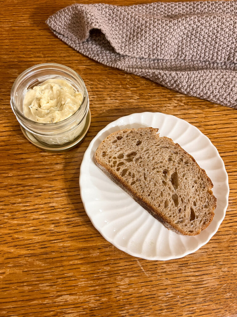 brown butter spread in a mason jar beside a slice of sourdough bread on a plate on a wooden table