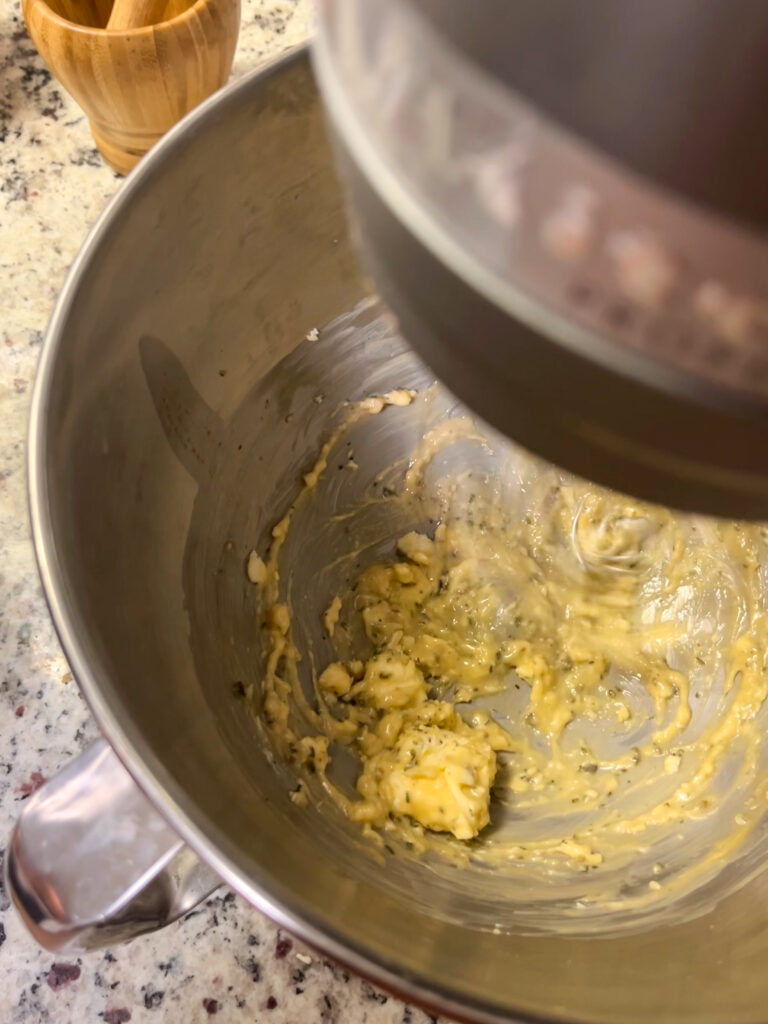 stainless steel mixing bowl with butter and herbs on a quartz countertop