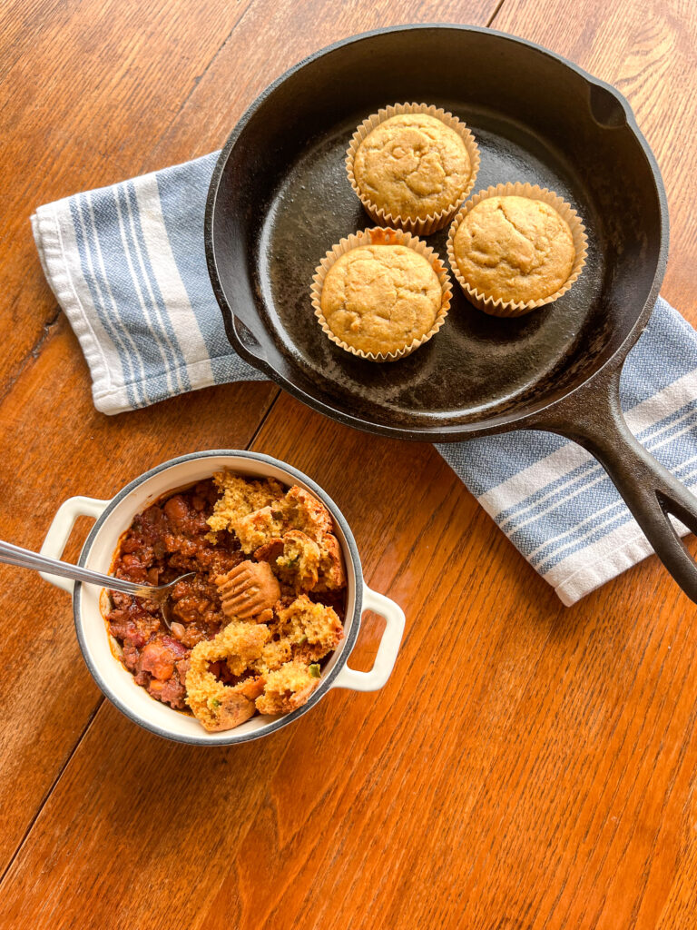small dutch oven of chili with a cast iron skillet of cornbread muffins on a kitchen table