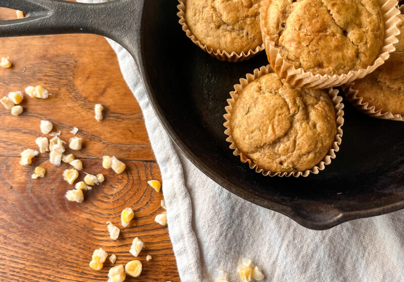 Cornbread muffins in a cast iron skillet with corn and a towel on a kitchen table