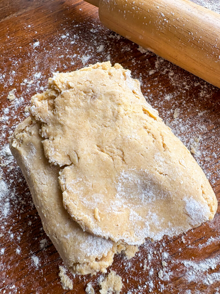 biscuit dough folded with flour and a wooden rolling pin on a kitchen table