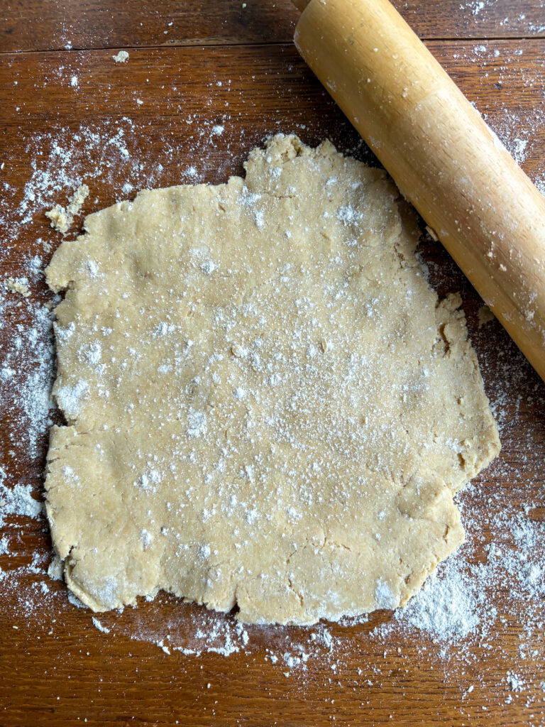 rolled out biscuit dough on a kitchen table with flour and a wooden rolling pin