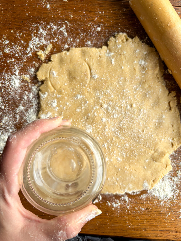 biscuit dough on a kitchen table with a mason jar and a wooden rolling pin