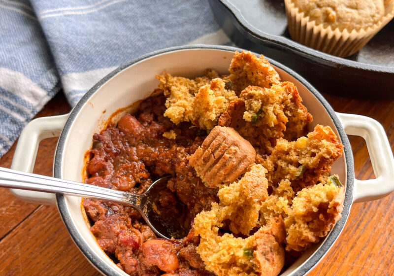 bowl of chili in a tiny white dutch oven with cornbread in a skillet on a kitchen table