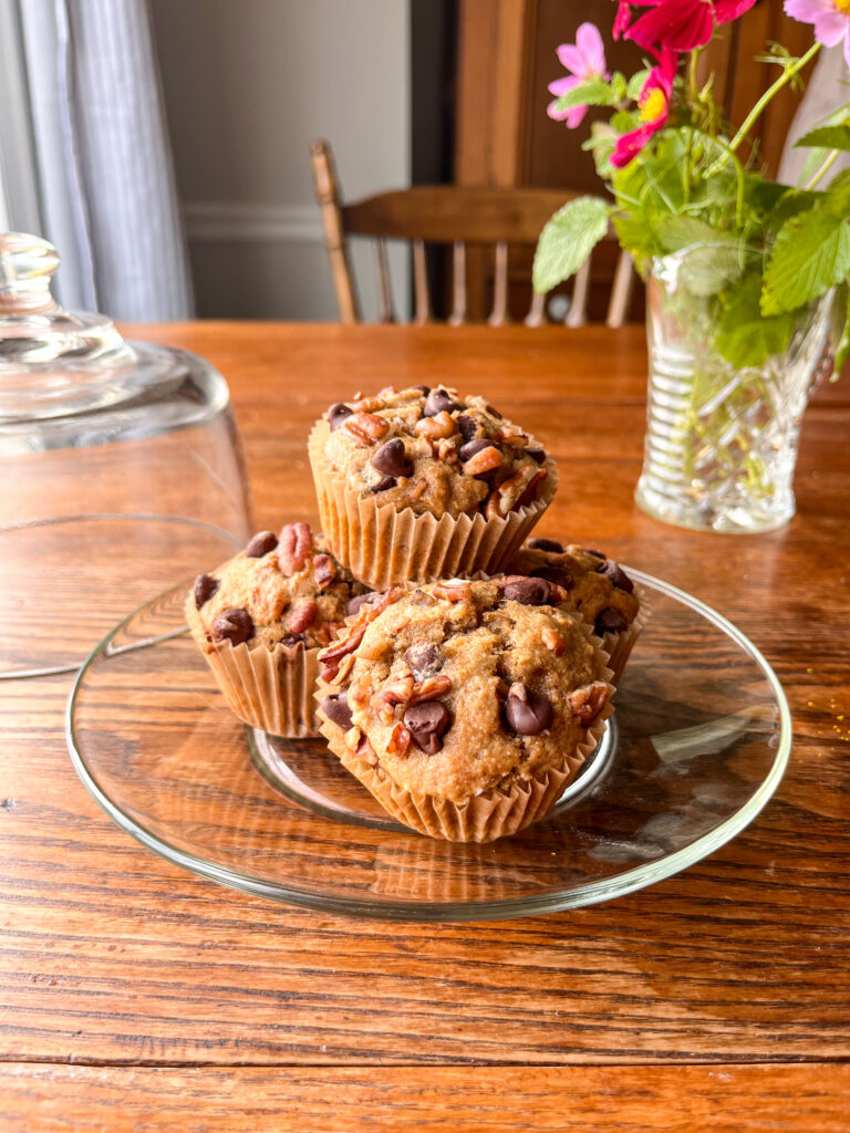 glass plate on a kitchen table with banana bread muffins with a vase with mint behind it.