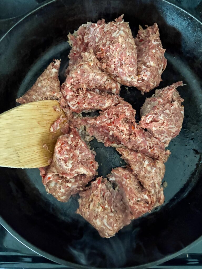 pork sausage in a cast iron skillet with a wooden spoon