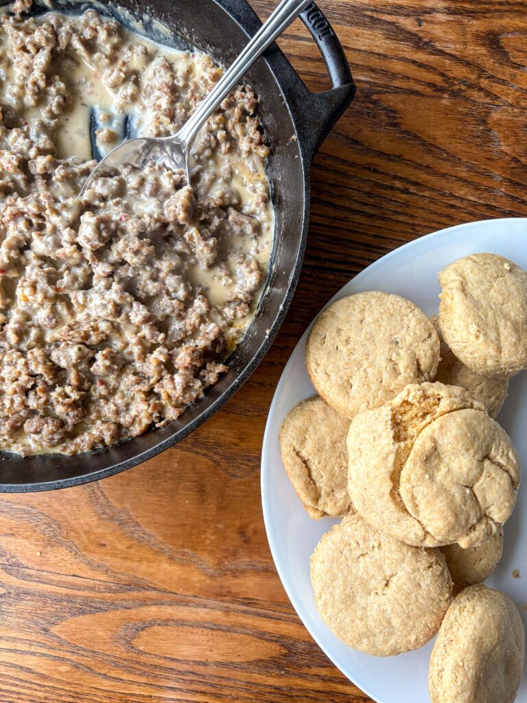 cast iron skillet with southern sausage gravy on a kitchen table beside a plate with biscuits on it