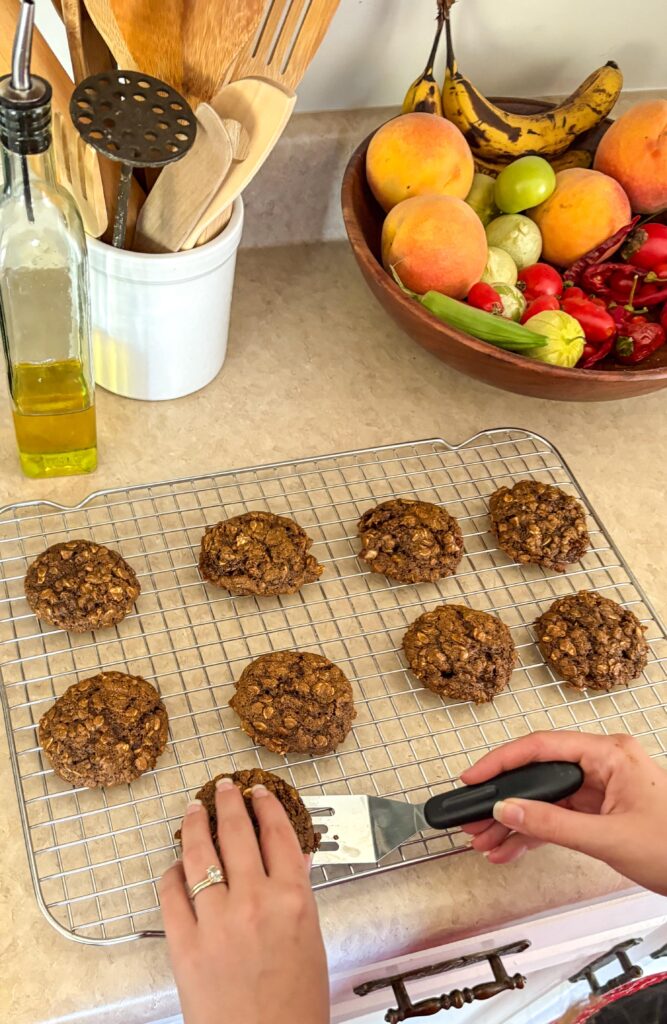 blackstrap molasses oatmeal cookies on a cooking rack on a kicthen counter with oil and bowl of veggies in the back