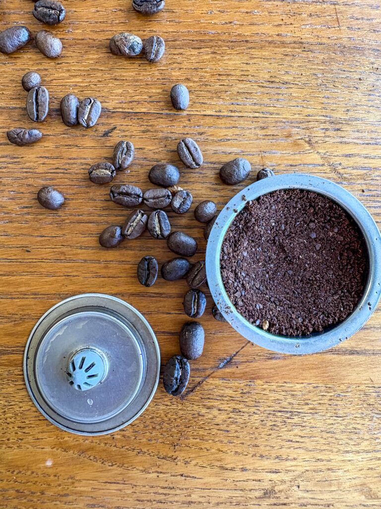 coffee ground in a stainless steel pod with coffee beans on a kitchen table