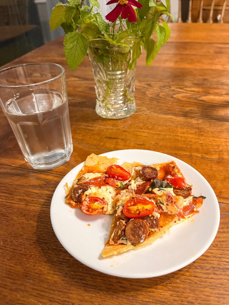 whole wheat sourdough discard pizza on a white plate on a kitchen table with a glass of water