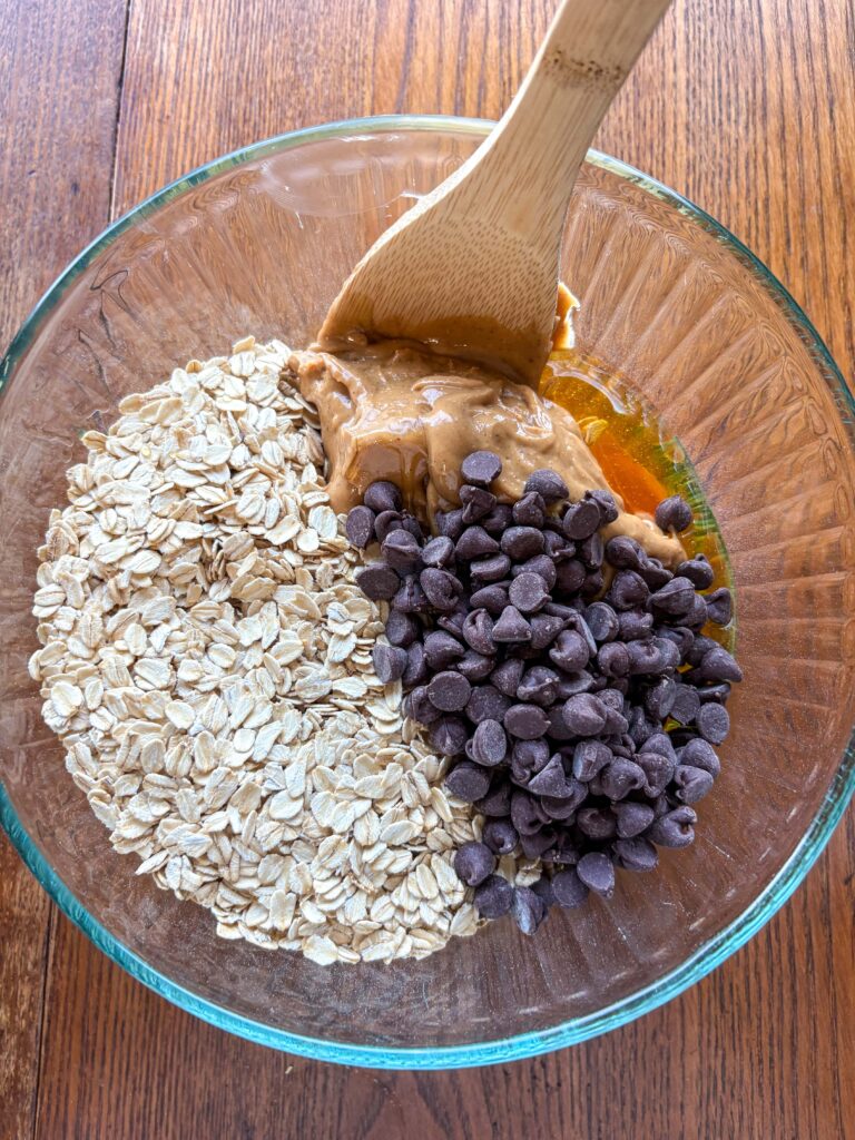 ingredients for peanut butter energy balls in a bowl on a kitchen table with a wooden spoon