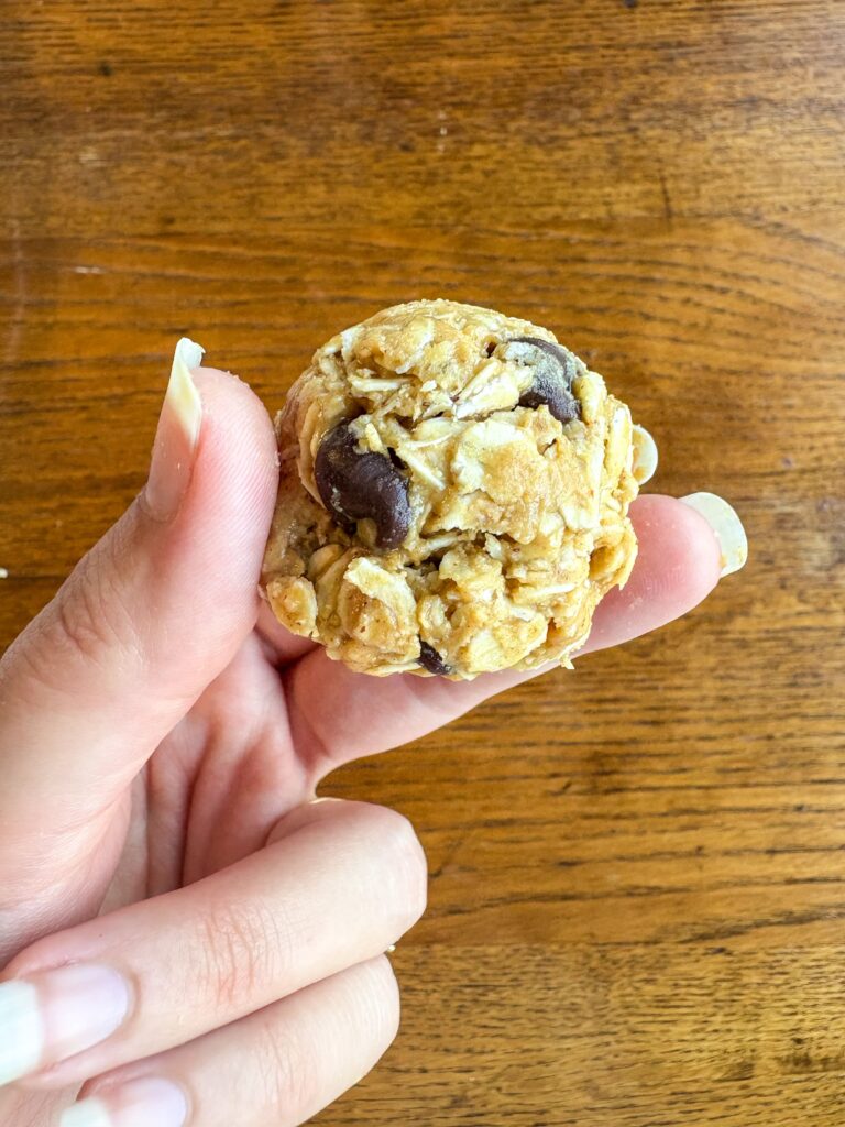 peanut butter energy ball in a woman's hand in front of a kitchen table