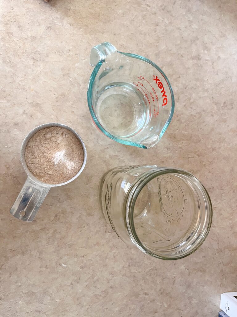 kitchen counter with mason jar, fresh milled flour, and water in a measuring cup