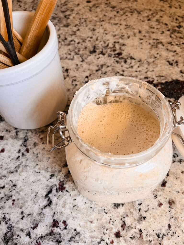 jar of sourdough starter on a kitchen counter with kitchen crock